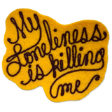 A yellow felt patch with dark brown embroidered text reading 'My loneliness is killing me' on a plain white background.