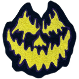 A chainstitch patch shaped like a jack-o'-lantern face, featuring a bright yellow textured design with a dark navy blue border and purple stitched outlines, isolated on a white background.