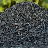 A close-up pile of dark, charred plant material, with a soft green blurred background.