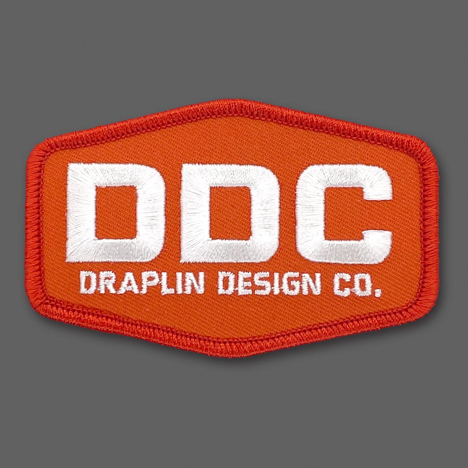 Draplin Design Company emblem in white and orange embroidery.