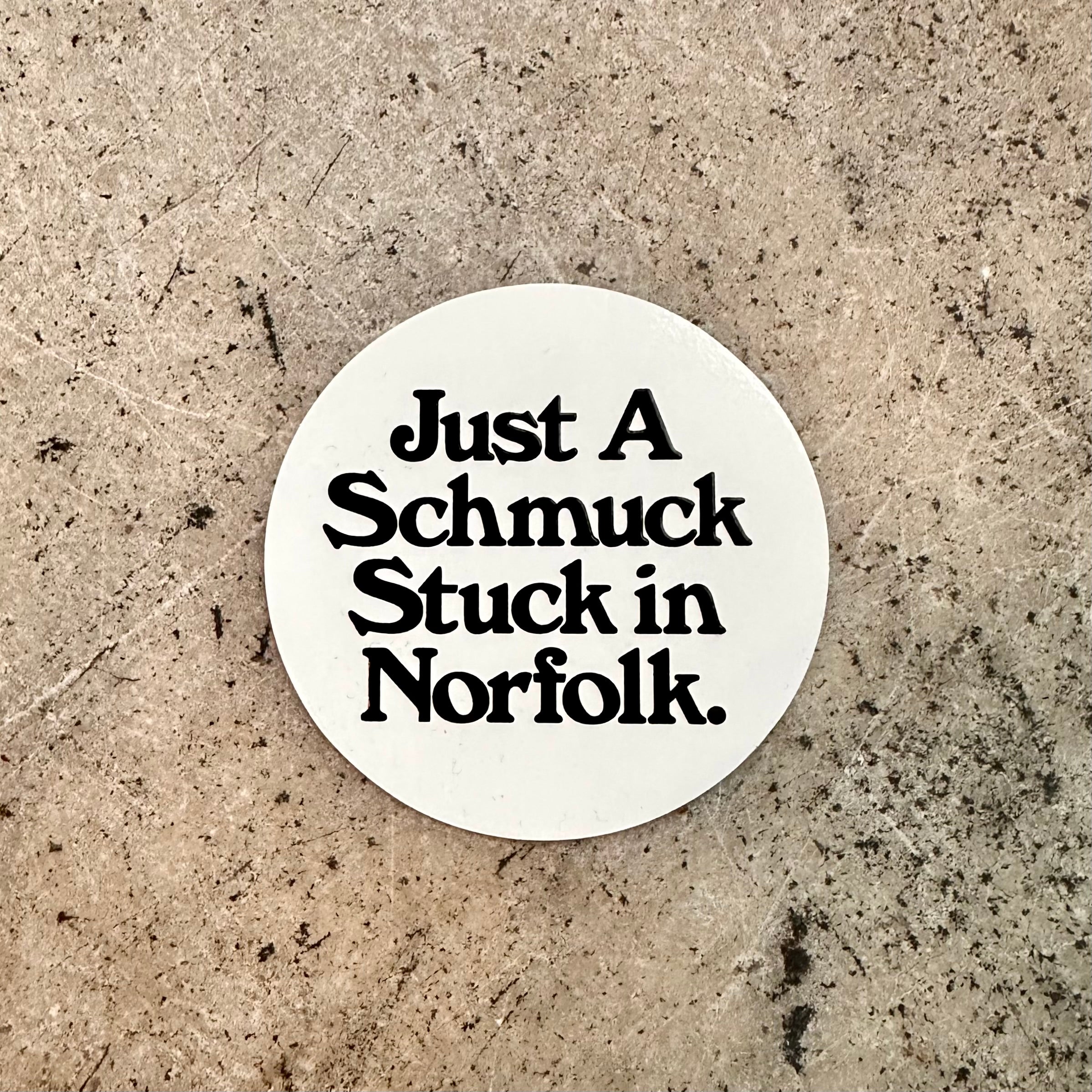 Screen printed vinyl sticker with black text on a white background reading "Just A Schmuck Stuck in Norfolk."