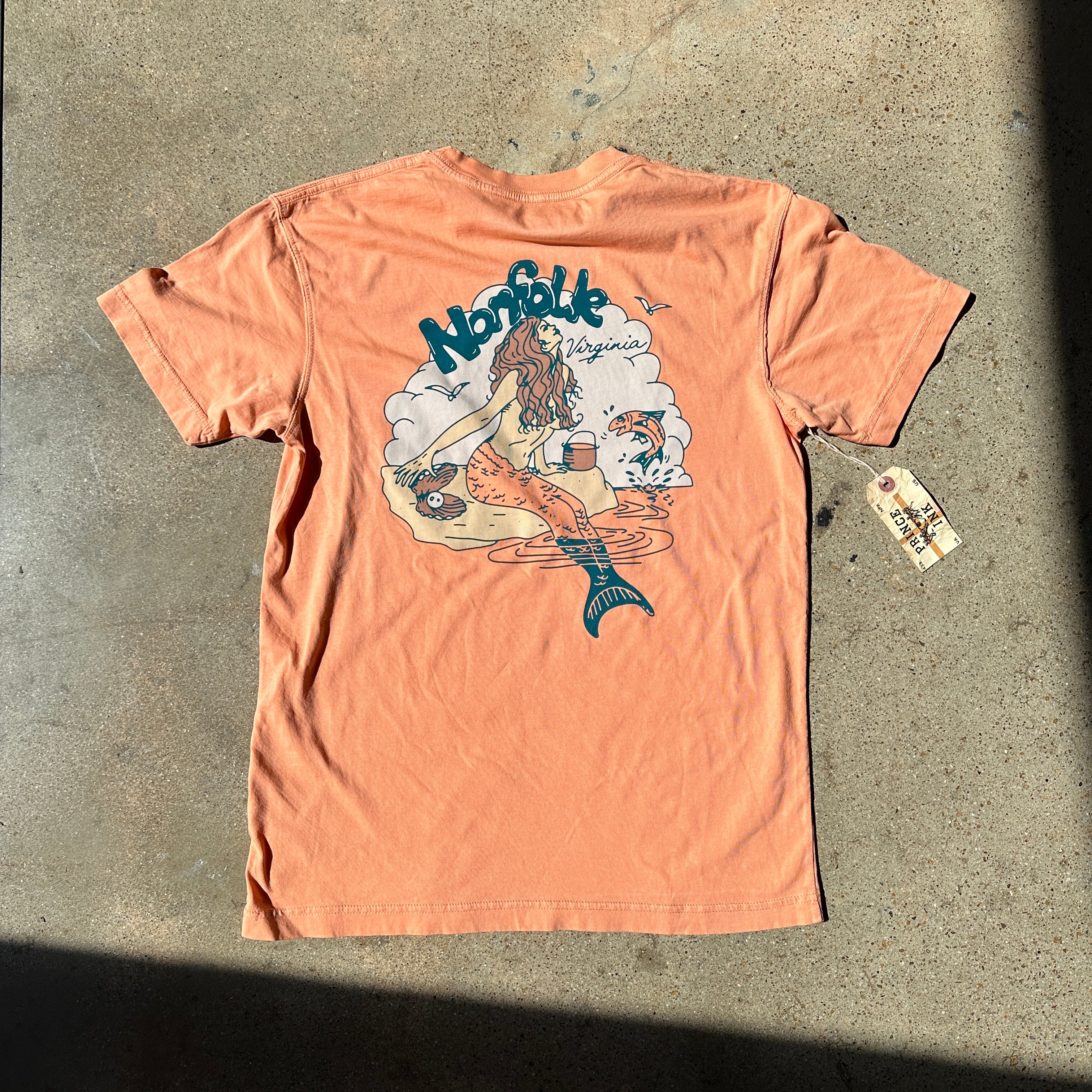 Back of an orange t-shirt printed with a vintage mermaid design including Norfolk Virginia