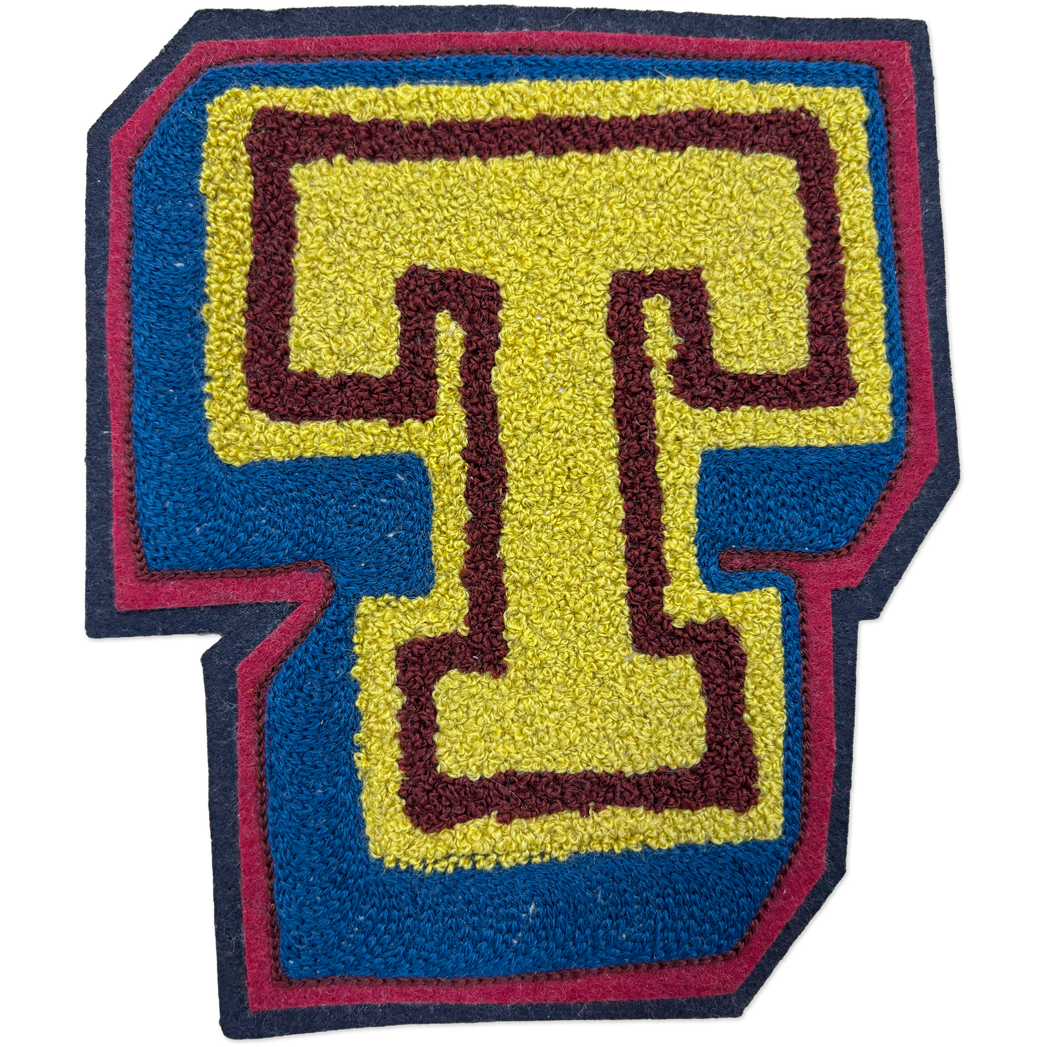 A hand-made chainstitch patch shaped like the letter T, featuring a yellow center with a dark burgundy outline, surrounded by a blue border and a dark navy outer edge.