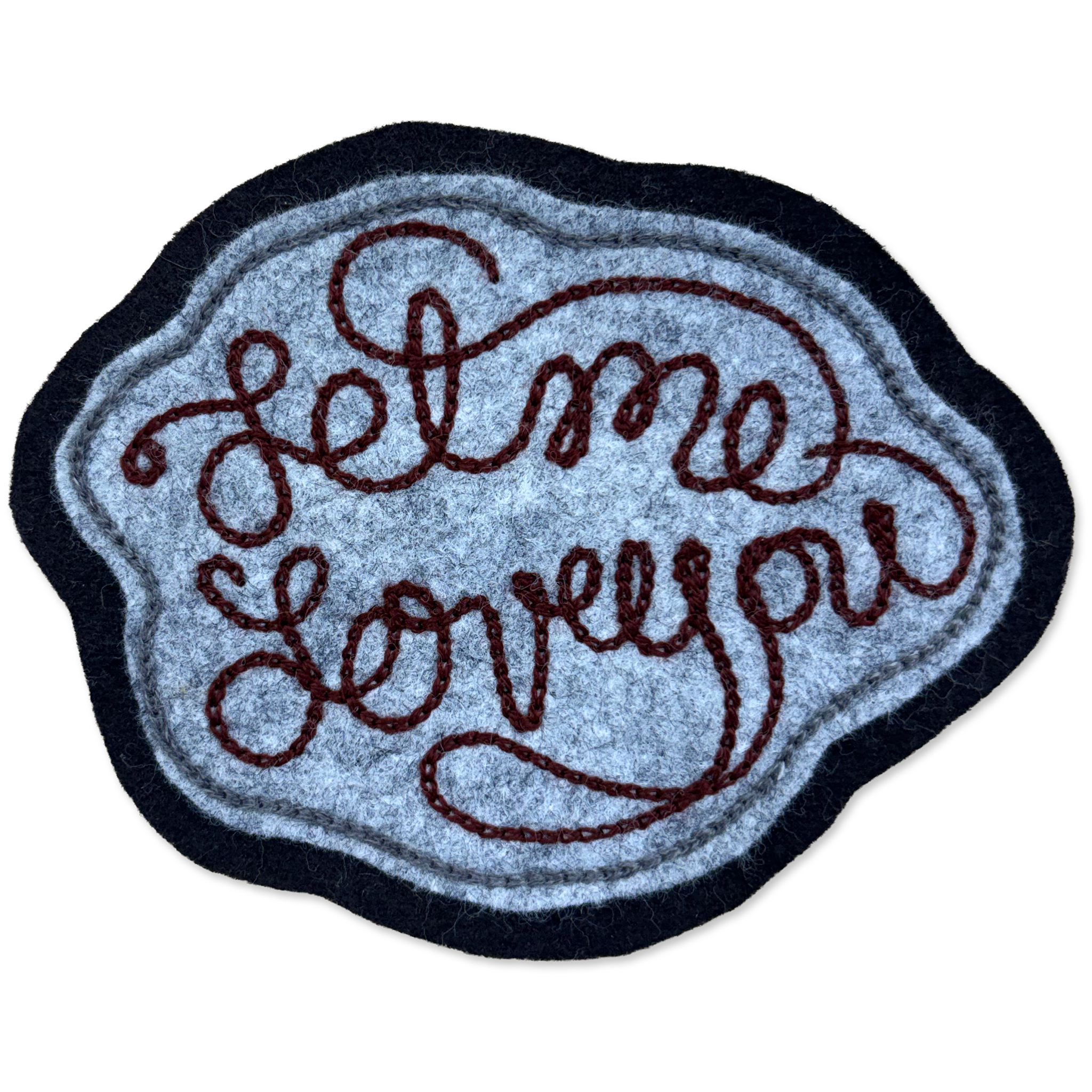 A felt patch with the phrase 'Let me love you' in dark brown cursive lettering, featuring a textured light blue center, a dark navy blue border, and a thin light blue inner border, shown on a plain white background.