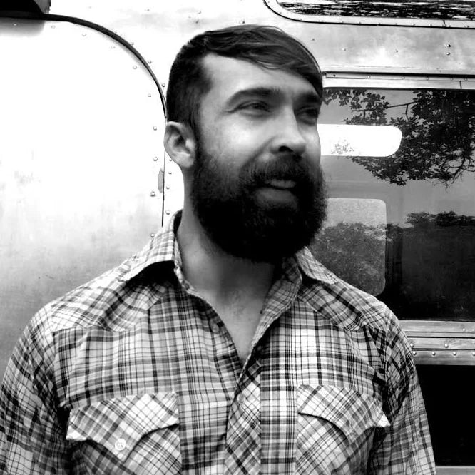 Man with a beard wearing a plaid shirt in front of a vintage vehicle