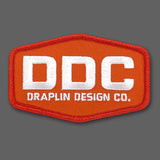 Draplin Design Company emblem in white and orange embroidery.